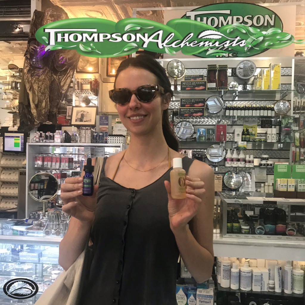 a lady standing inside of Thompson Alchemists holding 2 Thompson Alchemists products Thompson ALchemsits essential oil and body wash