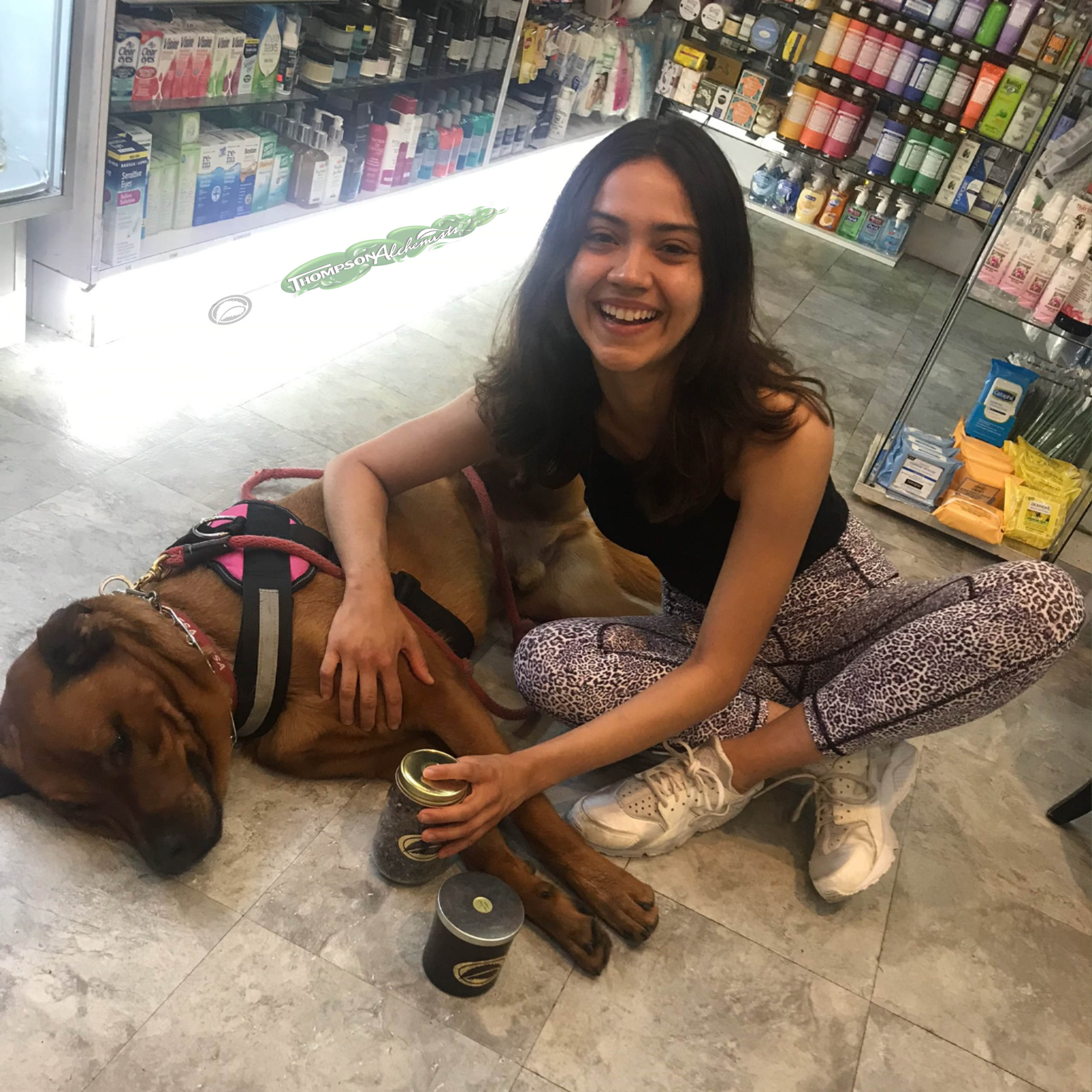 a picture of REGO the dog relaxing and with his friend who is holding holistic bath salts and a thompson alchemists candle